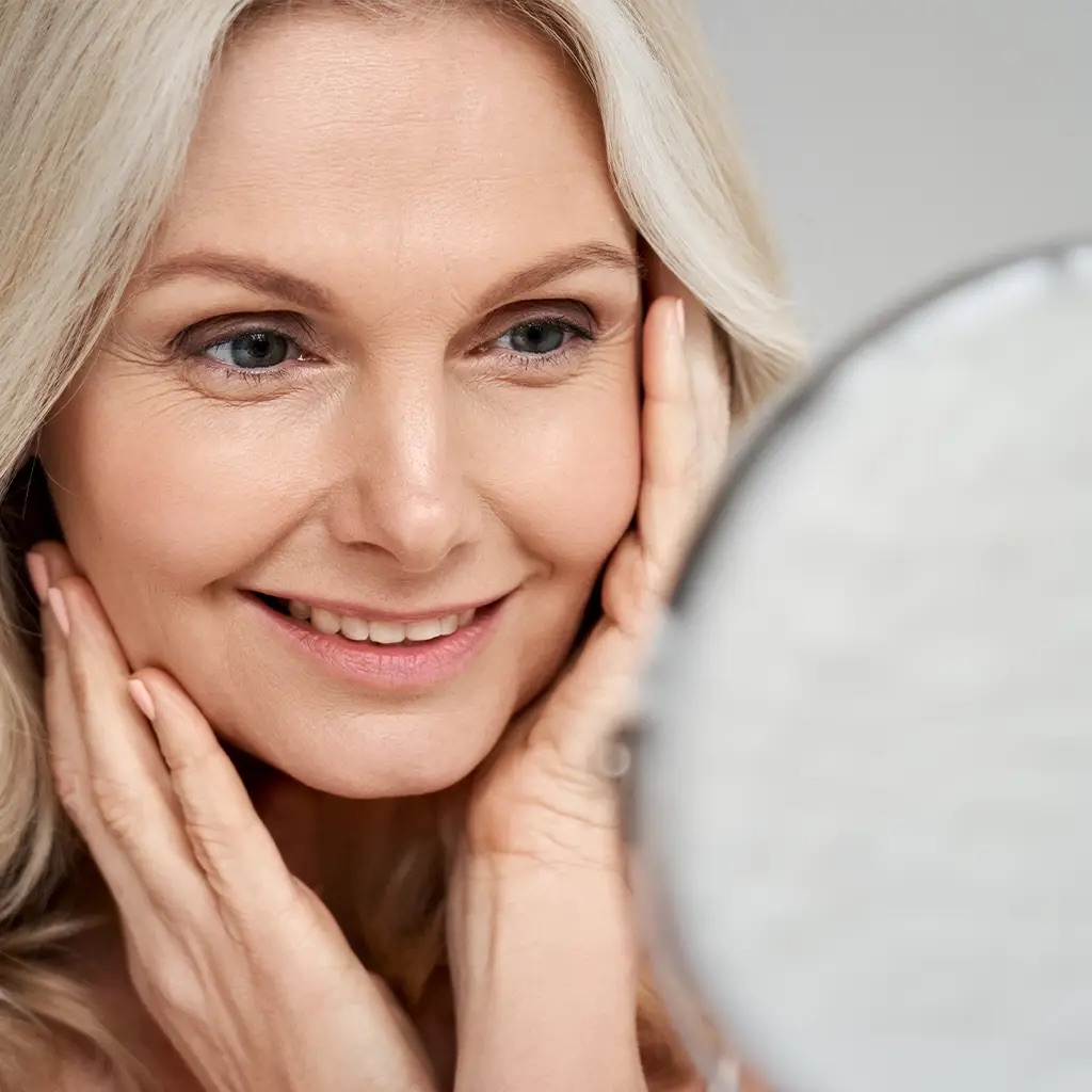 A woman looking at her reflection in a hand mirror, smiling.